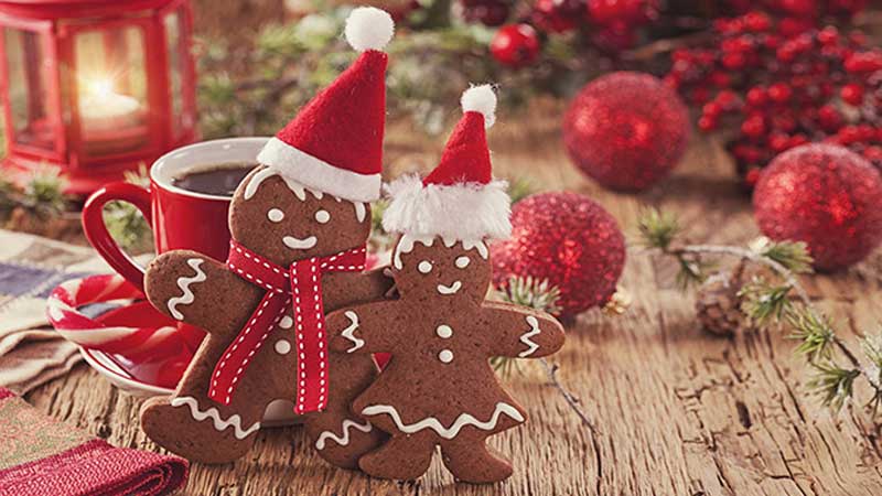Gingerbread man and woman cookies wearing Santa hats beside a mug of coffee