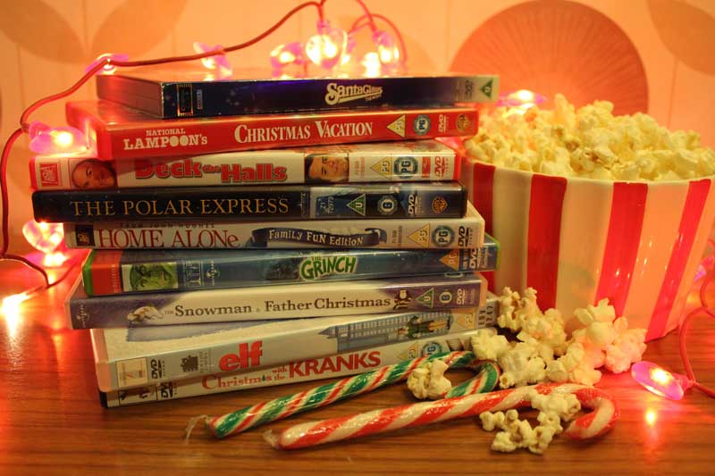 Stack of classic holiday movie DVDs next to a bowl of popcorn and candy canes