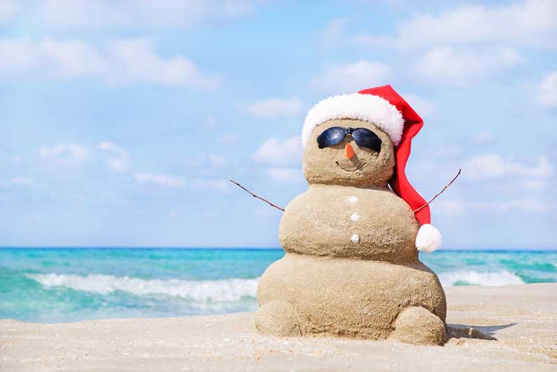 Snowman sculpted from sand wearing a Santa hat and sunglasses on a sunny beach