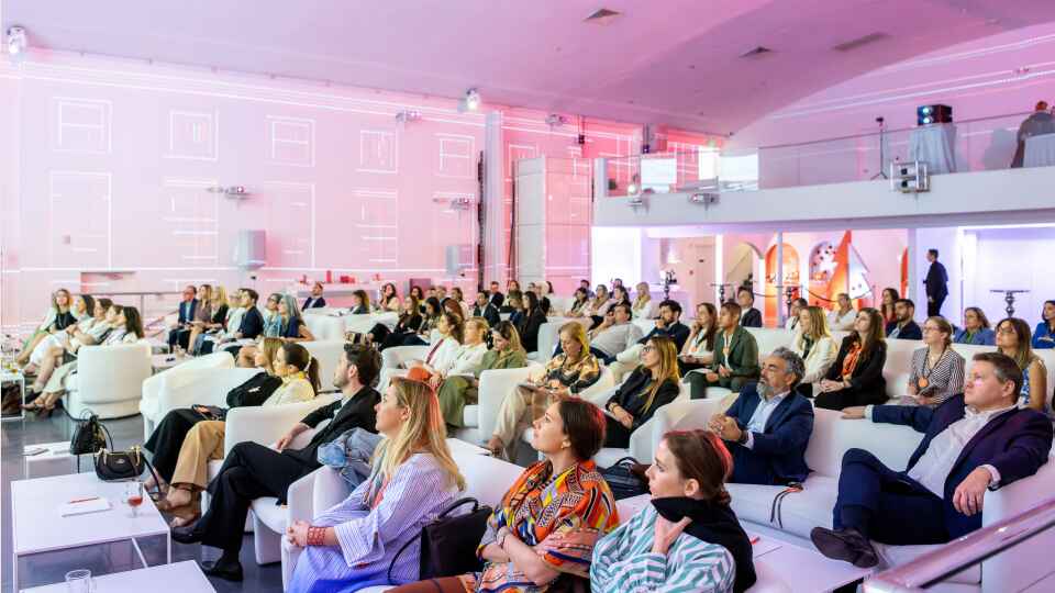 Corporate audience seated in white lounge furniture under pink lighting at a Fortune 500 event produced by an event agency.