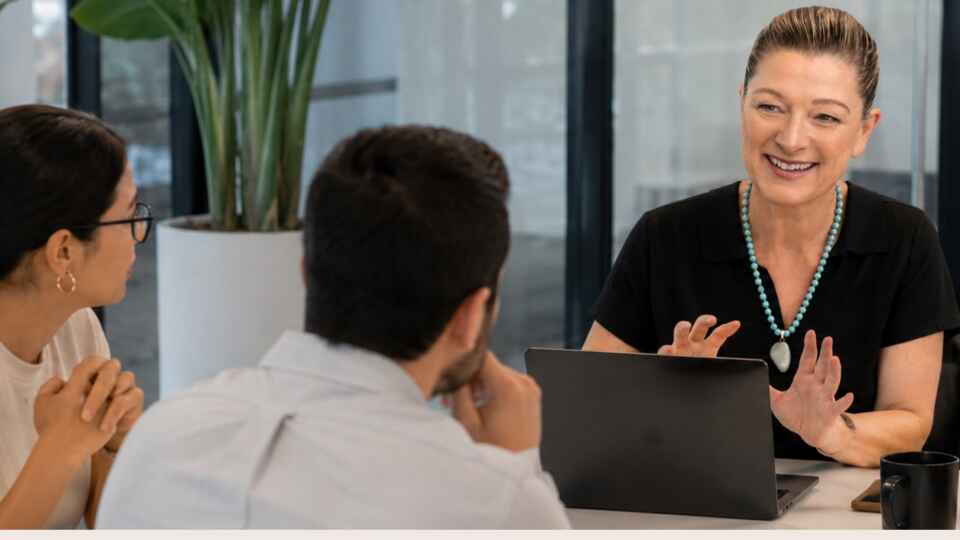 Event agency lead discussing production goals with two corporate clients around a laptop in a bright meeting room.